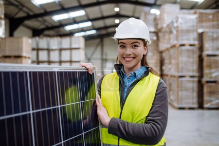 Foto de Trabajadora que lleva panel solar en almacén o fábrica. fabricante de paneles solares, fabricación solar. - Imagen libre de derechos