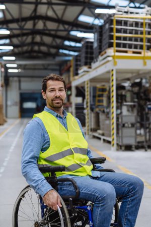 Téléchargez les photos : Homme en fauteuil roulant travaillant dans une usine industrielle moderne. Concept de travailleurs handicapés, lieu de travail accessible pour les employés à mobilité réduite. - en image libre de droit