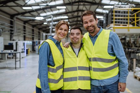 Portrait of young man with Down syndrome and his colleagues working in warehouse, holding around shoulders. Concept of workers with disabilities and support in workplace.