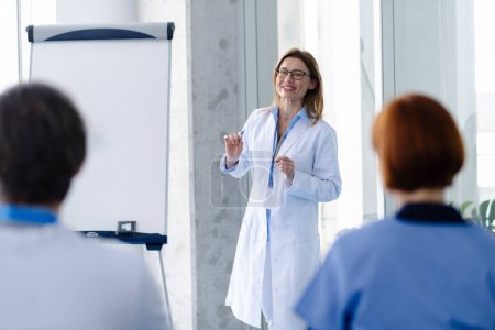 Photo for Female doctor as speaker at conference for group of healtcare workers, medical team sitting and listening presenter. Medical experts attending an education event, seminar in board room. - Royalty Free Image