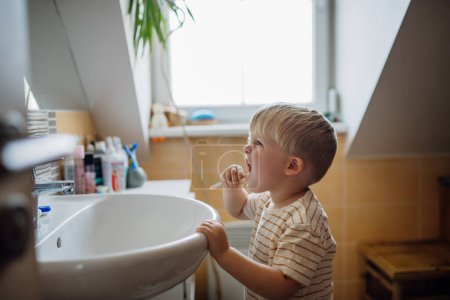 Foto de El niño pequeño cepillándose los dientes por la mañana, sin ayuda. Higiene dental matutina para niños pequeños. - Imagen libre de derechos