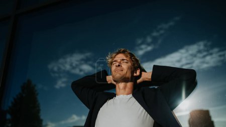 Photo for Portrait of handsome mature man with blond hair and closed eyes, standing outdoors in the city, in front of reflective wall. - Royalty Free Image