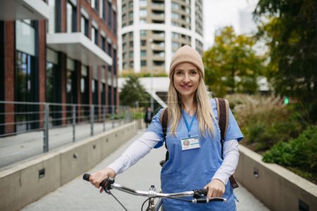Foto de Hermosa enfermera viajando por la ciudad en bicicleta. viajero médico de la ciudad que viaja desde el trabajo en bicicleta después de un largo día de trabajo en la clínica. - Imagen libre de derechos
