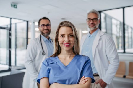 Photo for Portrait of female doctor standing in front of male colleagues. Beautiful nurse in uniform, standing in modern private clinic, looking at camera. - Royalty Free Image