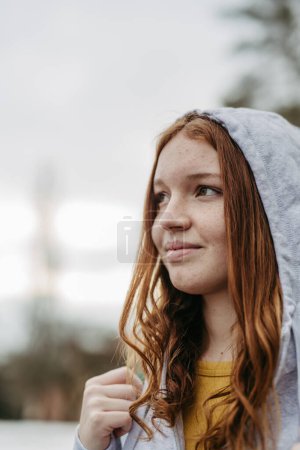 Foto de Retrato de hermosa cabeza roja gen z chica al aire libre. Chica con pelo de cobre, pecas con capucha en la cabeza. - Imagen libre de derechos