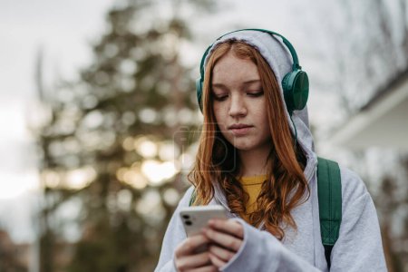 Photo for Portrait of teenage girl looking at her smartphone, feeling sad, anxious, alone. Cyberbullying, girl is harassed, threated online. - Royalty Free Image