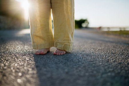 Foto de Primer plano de las niñas piernas descalzas en traje de verano a pie durante las vacaciones de verano, con pantalones de lino amarillo. - Imagen libre de derechos