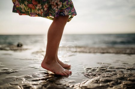 Foto de Primer plano de las niñas piernas saltando en la playa de arena. Descalzo feliz chica en vestido de verano divertirse. - Imagen libre de derechos