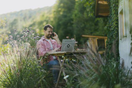 Téléchargez les photos : Homme travaillant dans le jardin sur ordinateur portable, appel téléphonique sur smartphone. Homme d'affaires travaillant à distance de la maison de plein air, pensant à de nouvelles affaires ou idée créative. - en image libre de droit