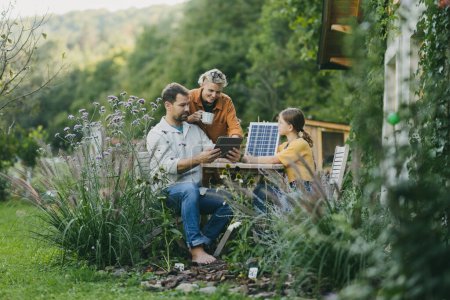 Foto de Los padres con la hija sentada al aire libre en el jardín, con el modelo de panel solar, el aprendizaje de la energía solar. Energía solar y estilo de vida sostenible de la familia joven. Concepto de energía verde y - Imagen libre de derechos