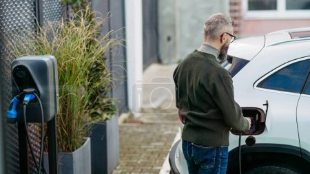 Photo for Businessman charging electric car before going to office. An electric vehicle charging station in front of the office building. Charging at work, workplace. - Royalty Free Image