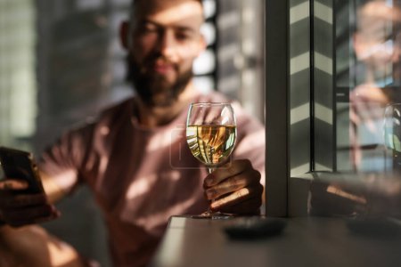 Junger Mann blickt auf ein Glas mit Weißwein, Neujahrsvorsätze, trinkt weniger Alkohol, gesunder Lebensstil ohne alkoholische Getränke.
