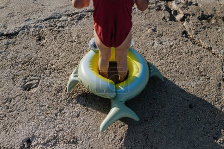 Foto de Primer plano de niña pequeña en traje de baño rojo de pie anillo de juguete inflable, mirando al mar. - Imagen libre de derechos