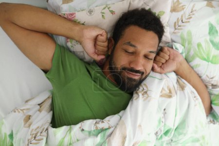 Foto de Vista superior del hombre feliz despertando en la cama, estirando los brazos, sonriendo por la mañana. - Imagen libre de derechos