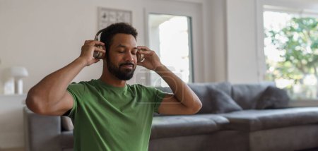 Photo for Young man with closed eyes, listening meditating music at home. Morning or evening workout routine, listening to music through wireless headphones. Banner with copyspace. - Royalty Free Image