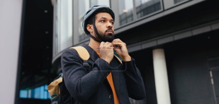 Photo for City commuter, businessman traveling from work to home on a bike, fastening helmet for safety. City lifestyle of single man. Banner with copyspace. - Royalty Free Image