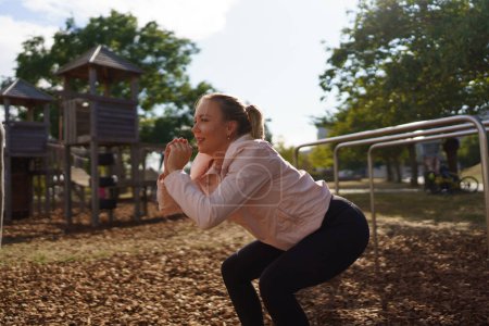 Seitenansicht einer Frau, die in einem städtischen Outdoor-Fitnessstudio Kniebeugen macht. Bewegung nach der Arbeit für eine gute psychische Gesundheit, körperliche Gesundheit, Stressabbau und Stimmungsaufhellung.