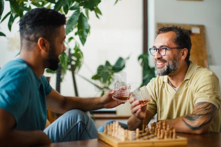 Téléchargez les photos : Meilleurs amis jouant aux échecs ensemble, buvant du whisky et parlant. Concept d'amitié masculine et de bromance. - en image libre de droit