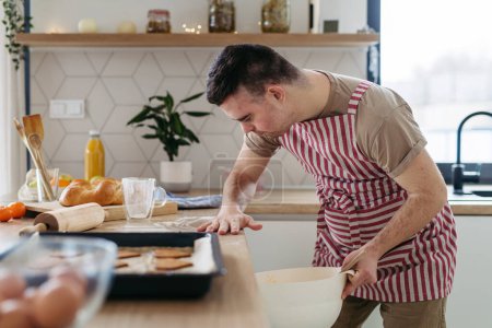 Téléchargez les photos : Un jeune homme trisomique qui fait des biscuits à la maison. routine quotidienne pour les hommes atteints de trisomie 21 trouble génétique. - en image libre de droit