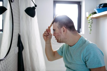 Téléchargez les photos : Vue latérale du jeune homme avec le syndrome du duvet dans la salle de bain, peigner ses cheveux. - en image libre de droit