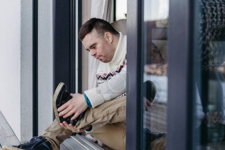 Photo for Portrait of young man with Down syndrome putting on shoes, sitting on the floor. - Royalty Free Image