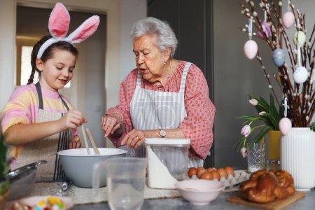 Photo for Grandmother with grandaughter preparing traditional easter meals, baking cakes and sweets. Passing down family recipes, custom and stories. Concept of family easter holidays. - Royalty Free Image