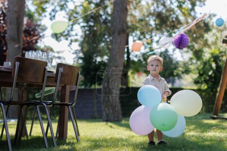 Foto de Niño sosteniendo globos de colores en la fiesta de cumpleaños al aire libre. Fiesta de cumpleaños jardín para niños. - Imagen libre de derechos