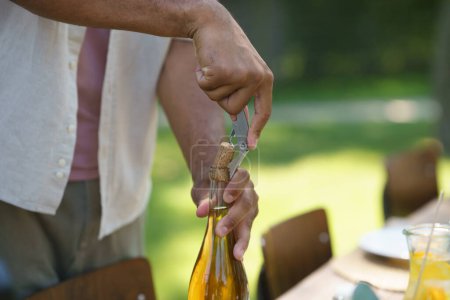 Close up of hands opening wine with wine opener at summer garden party.