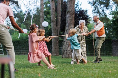 Foto de Los abuelos tienen un tira y afloja con sus nietos. Juegos divertidos en la fiesta del jardín familiar. - Imagen libre de derechos
