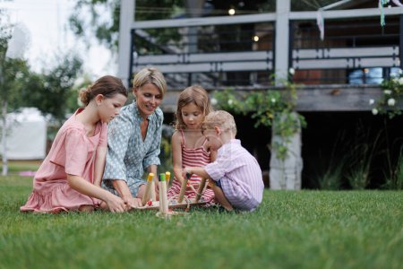 Photo for Woman playing with three kids in the garden, outdoor garden games, sitting on grass. - Royalty Free Image
