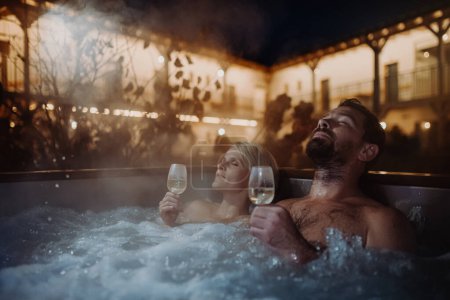 Photo for Beautiful mature couple relaxing in outdoor hot tub, drinking champagne, enjoying romantic wellness weekend in the spa. Concept of Valentines Day. - Royalty Free Image