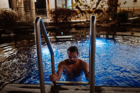Foto de Hombre maduro saliendo de la piscina al aire libre por la noche, disfrutando de la calma y la piscina vacía. Fin de semana de bienestar en el hotel. - Imagen libre de derechos