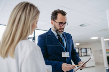 Portrait of pharmaceutical sales representative talking with doctor in medical building. Ambitious male sales representative in suit presenting new medication on tablet.
