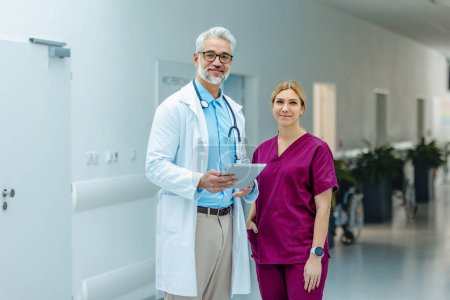 Téléchargez les photos : Portrait de l'équipe médicale, médecin et belle infirmière en uniforme, debout dans le couloir de l'hôpital, regardant la caméra et souriant. - en image libre de droit