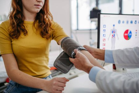 Doctor examining teenage girl, measuring blood pressure, using clinical blood pressure monitor. Concept of annual preventive health care for teenagers.