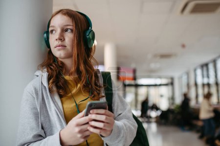 Téléchargez les photos : Adolescente qui attend dans le couloir de l'hôpital, écoutant de la musique via un casque. Patient adolescent venant à l'hôpital pour un examen. - en image libre de droit