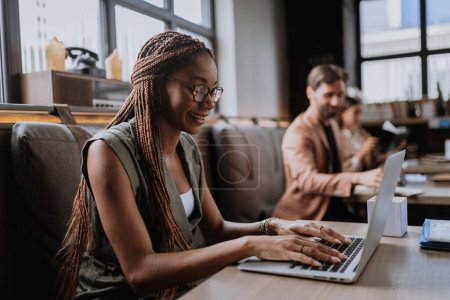 Photo for Beautiful businesswoman working on laptop in modern office. Group of freelancers working in shared work area. Concept of coworking, common workspaces for business, startups. Working remotely from - Royalty Free Image