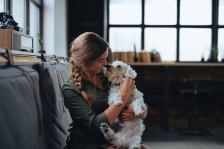 Téléchargez les photos : Portrait de belle jeune femme tenant son chien et souriant. Mignon chien blanc dans les bras du propriétaire aimant. Avec chien dans un café. - en image libre de droit