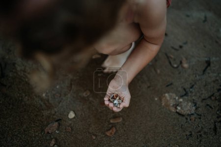 Foto de Primer plano de conchas marinas en la palma de los niños con dedos de ciruela. Sirviendo conchas en la arena. Concepto de vacaciones de verano por mar. - Imagen libre de derechos