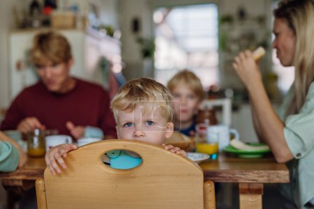 Foto de Familia joven desayunando juntos en la cocina casera. Desayuno o merienda antes de la escuela y el trabajo. Madre ayudando a su hijo menor. - Imagen libre de derechos