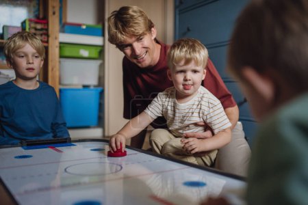Photo for Dad with three sons playing in kids room, air hockey. Concept of Fathers Day, and fatherly love. Real family, real people at home. - Royalty Free Image
