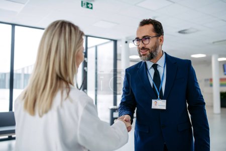 Portrait of pharmaceutical sales representative talking with doctor in medical building, clinic lobby. Ambitious male sales representative in suit shaking hand with female doctor.