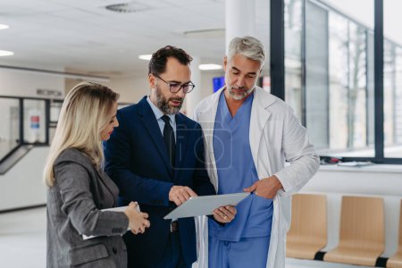 Photo for Pharmaceutical sales representative presenting new medication to doctors in medical building, presenting on tablet. Hospital managers of private medical clinic talking with doctor. Generous donor - Royalty Free Image