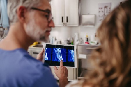 Foto de Médico mostrando una paciente hembra con resonancia magnética en la tableta, discutiendo el resultado de su prueba en la sala de emergencias. Problemas con la columna cervical, vértebras del cuello. - Imagen libre de derechos