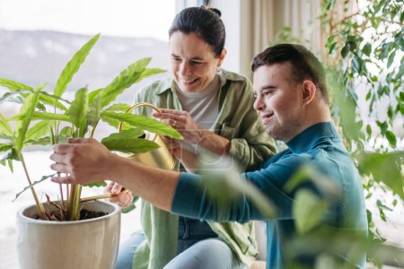 Photo for Top view of young man with Down syndrome with his mother at home, taking care of houseplants. Concept of love and parenting disabled child. - Royalty Free Image