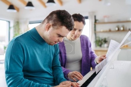 Photo for Young man with down syndrome and his mother playing on piano, making music at home. Practicing piano with music teacher. - Royalty Free Image