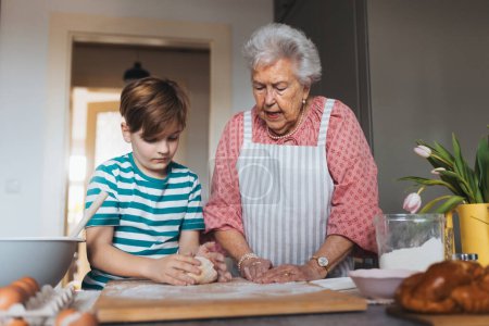 Photo for Grandmother with grandson preparing traditional easter meals, kneading dough for easter cross buns. Passing down family recipes, custom and stories. Concept of family easter holidays. - Royalty Free Image