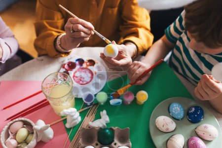 Photo for Close up of decorating easter eggs at home. Tradition of painting eggs with brush and easter egg dye. Concept of family easter holidays. - Royalty Free Image