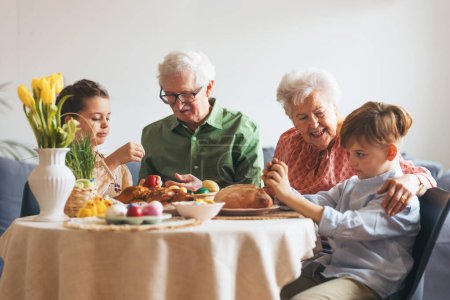 Foto de Abuelos con nietos comiendo el tradicional almuerzo de Pascua. Recreando tradiciones y costumbres familiares. Concepto de vacaciones familiares de Pascua. - Imagen libre de derechos