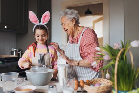 Grandmother with grandaughter preparing traditional easter meals, baking cakes and sweets. Passing down family recipes, custom and stories. Concept of family easter holidays.